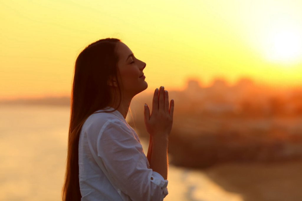 mulher em posição de reza em um lugar ao pôr do sol