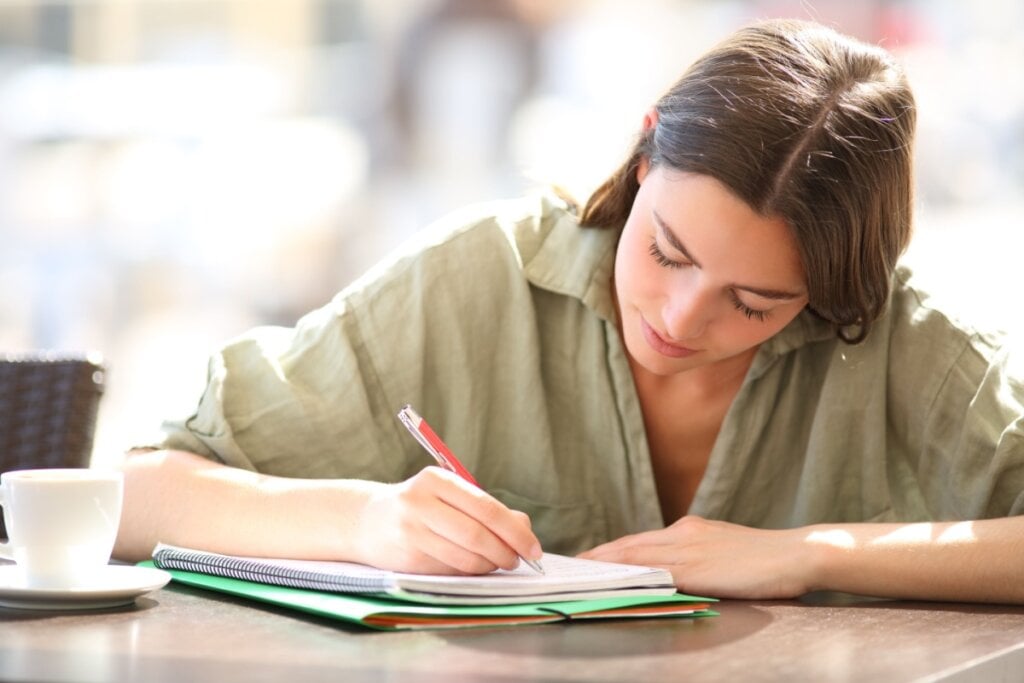 Jovem escrevendo com caneca em caderno