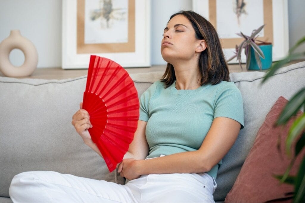 Mulher sentada em um sofá se abanando com um leque