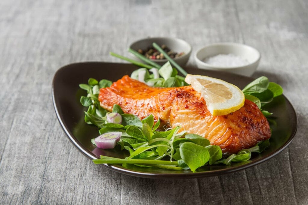 Salmão grelhado em cima de salada em um prato preto 