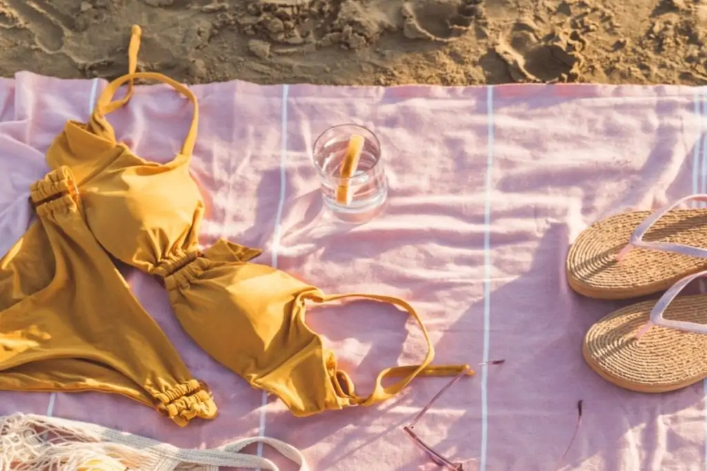 Biquíni amarelo em cima de pano rosa em areia da praia