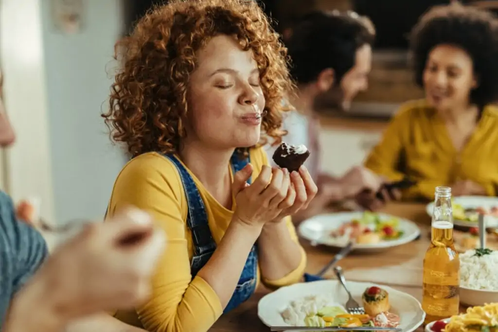 Mulher ruiva de olhos fechados comendo pedaço de bolo