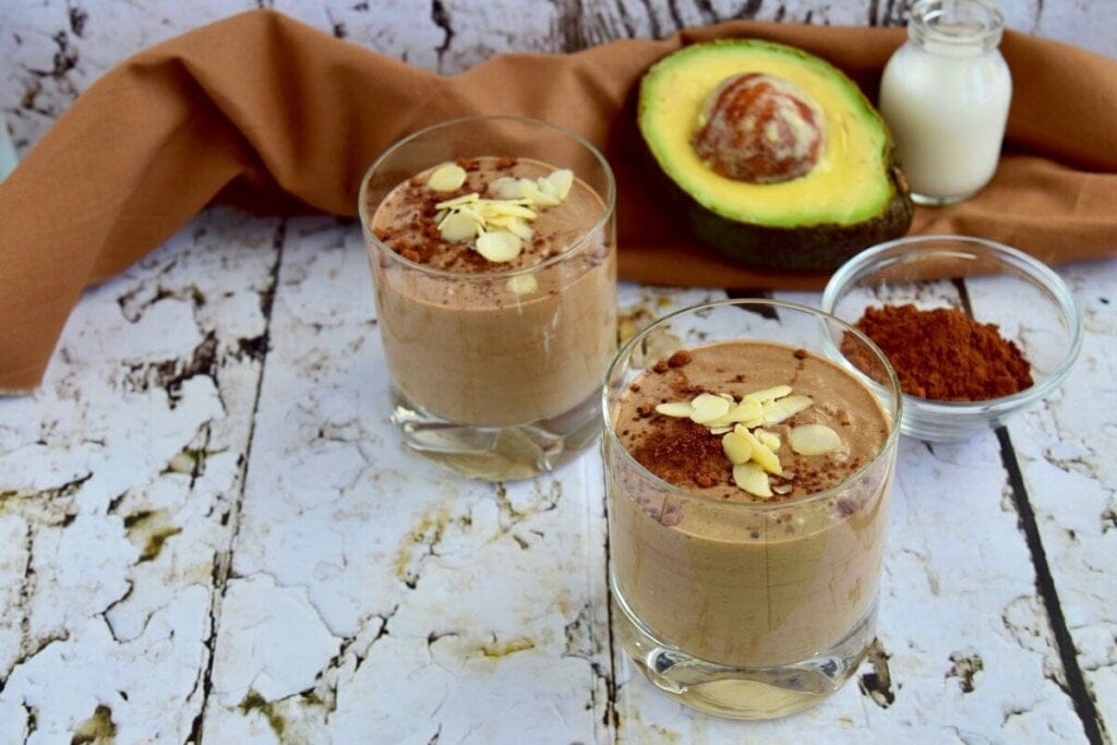 Dois copos com vitamina de abacate com chocolate decorados com aveia laminada e chocolate em pó