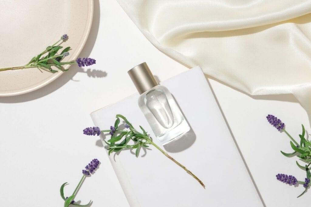 Vidro de perfume de alfazema com flores de alfazema ao redor em fundo branco