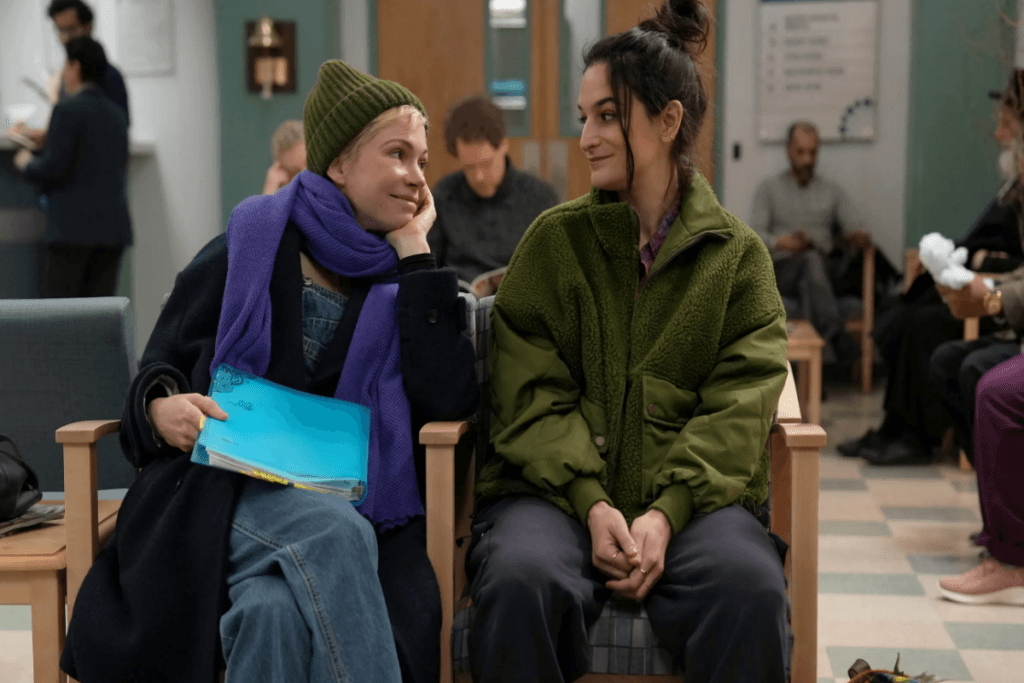 Duas mulheres com roupas de frio sentadas em sala de espera, uma olhando para outra sorrindo