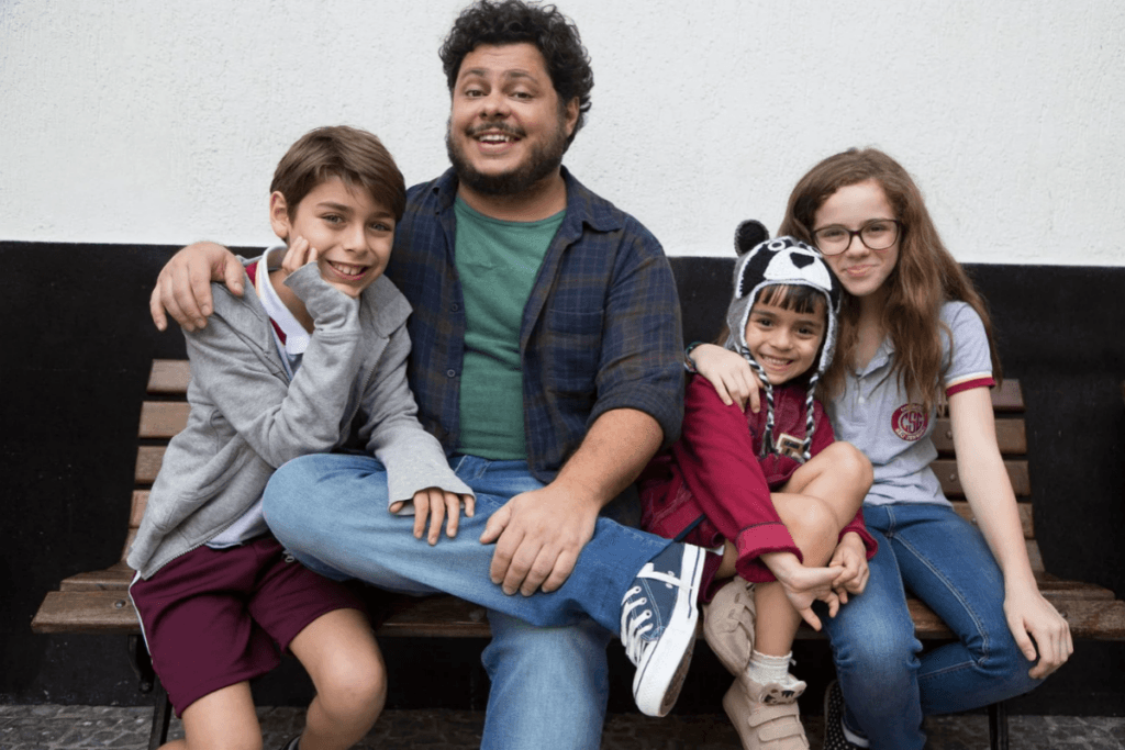 Imagem de homem sentado em banco com três crianças, duas meninas e um menino
