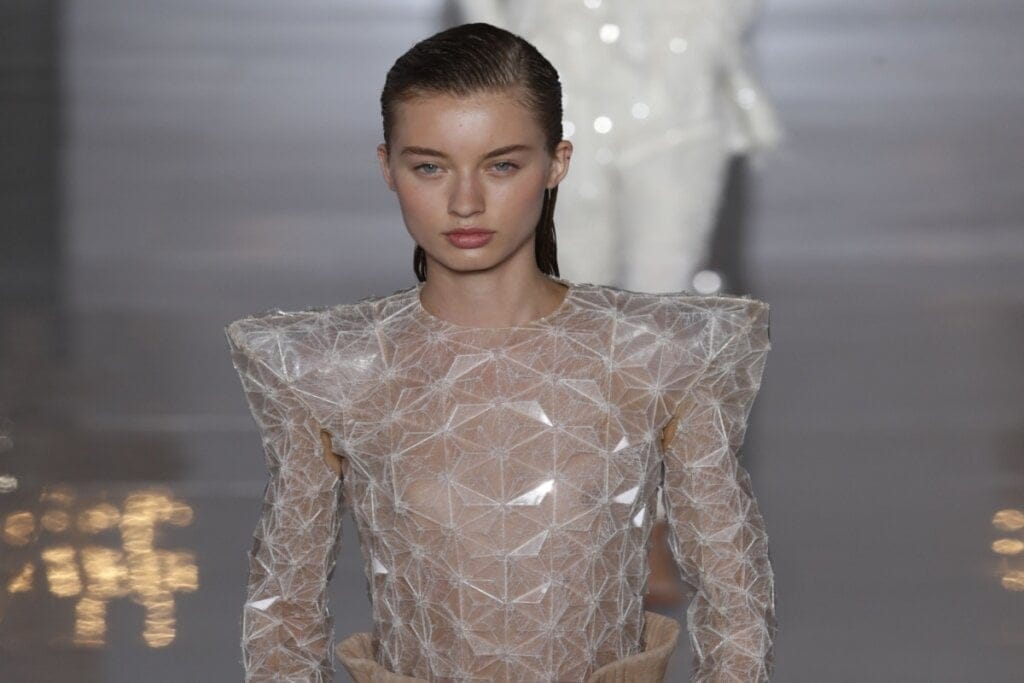 Modelo na passarela com cabelo estilo molhado e vestido com transparência geométrica