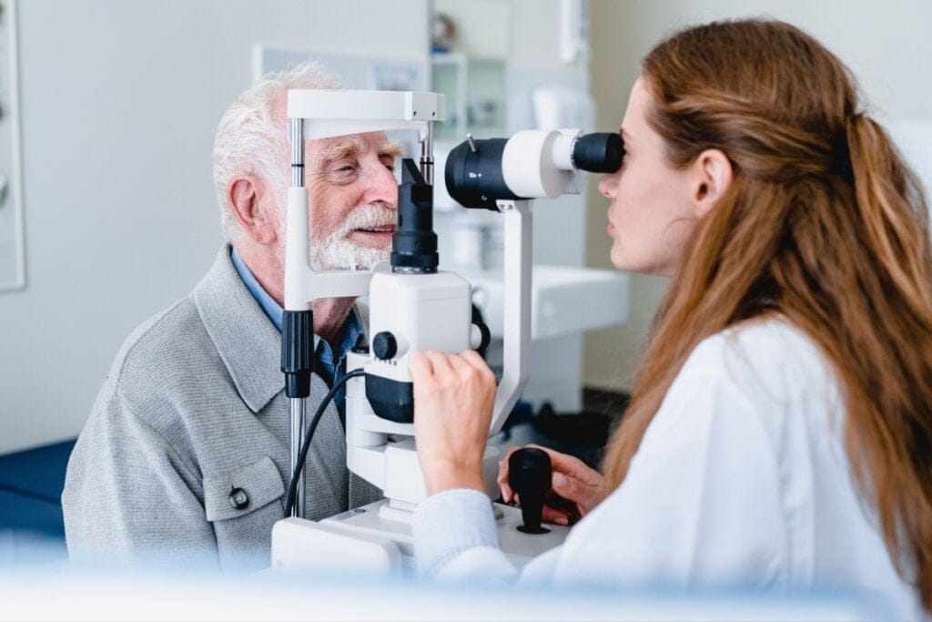 Homem idoso sentado e com a cabeça apoiada em aparelho enquanto oftalmologista examina o olho dele
