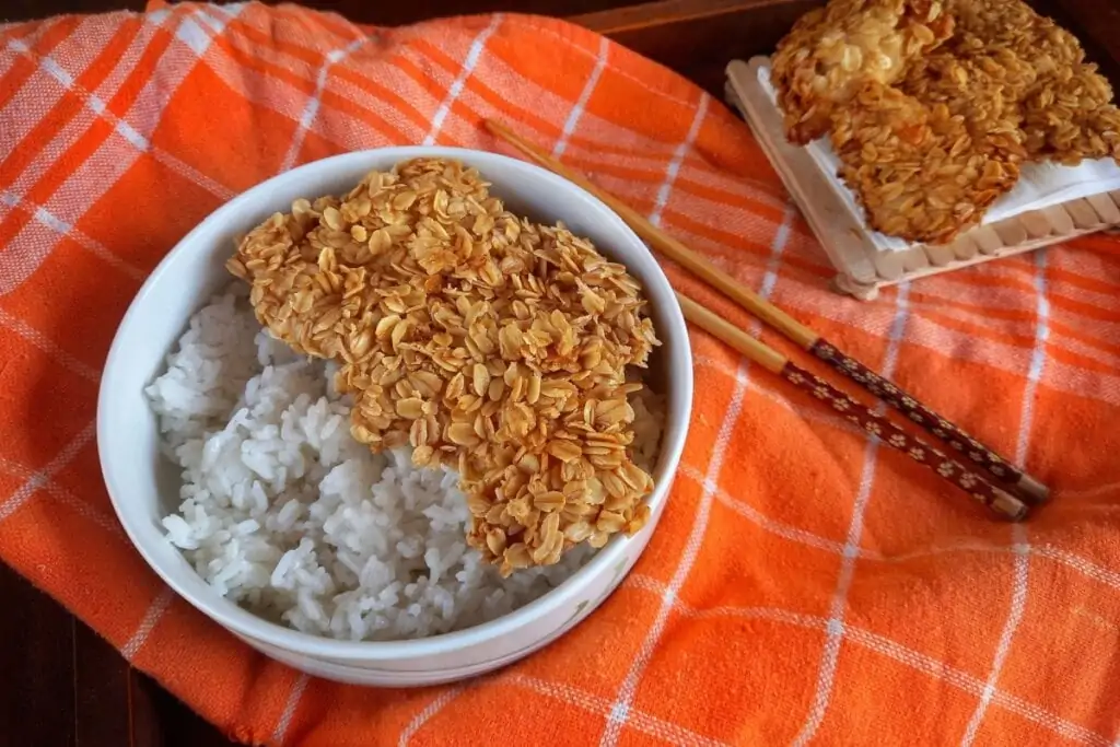 Filé de frango empanado com flocos de aveia dentro de um recipiente branco com arroz 