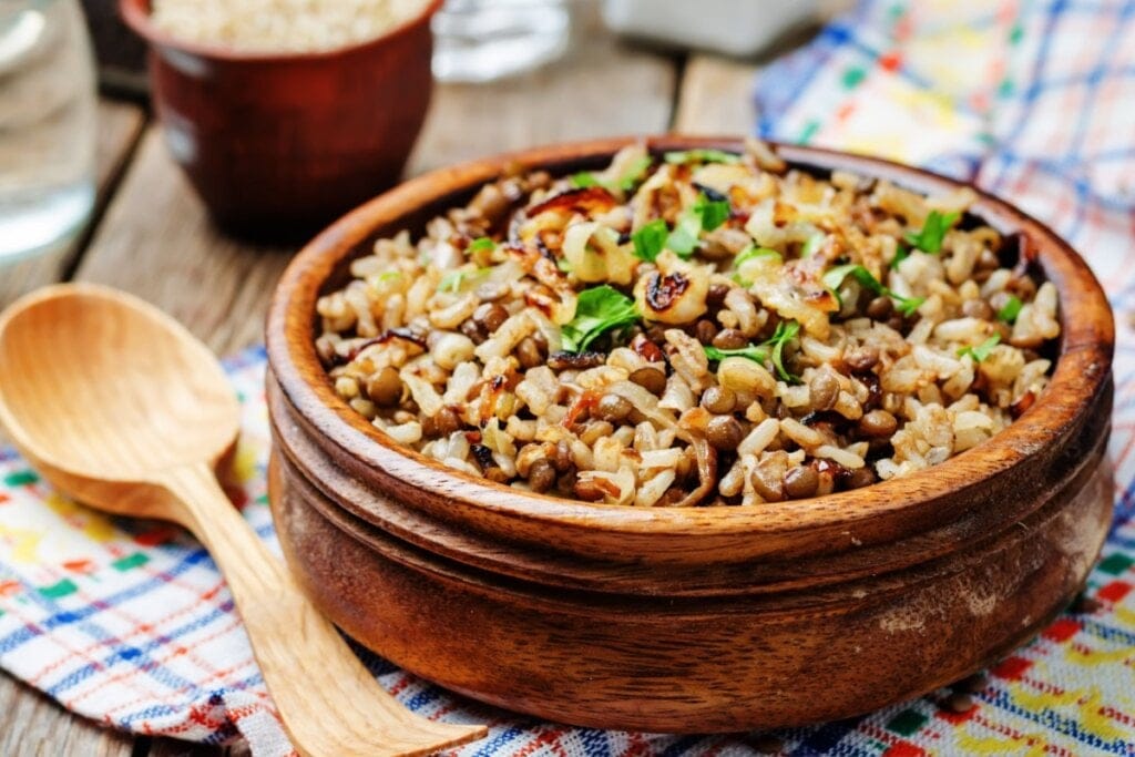 Arroz com lentilha e cebola servido em tigela de madeira em cima de mesa de madeira