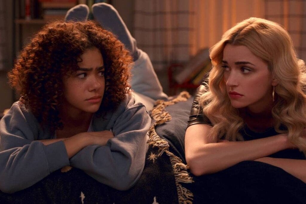 Ginny e Georgia deitadas de barriga para baixo em uma cama e olhando uma para a outra