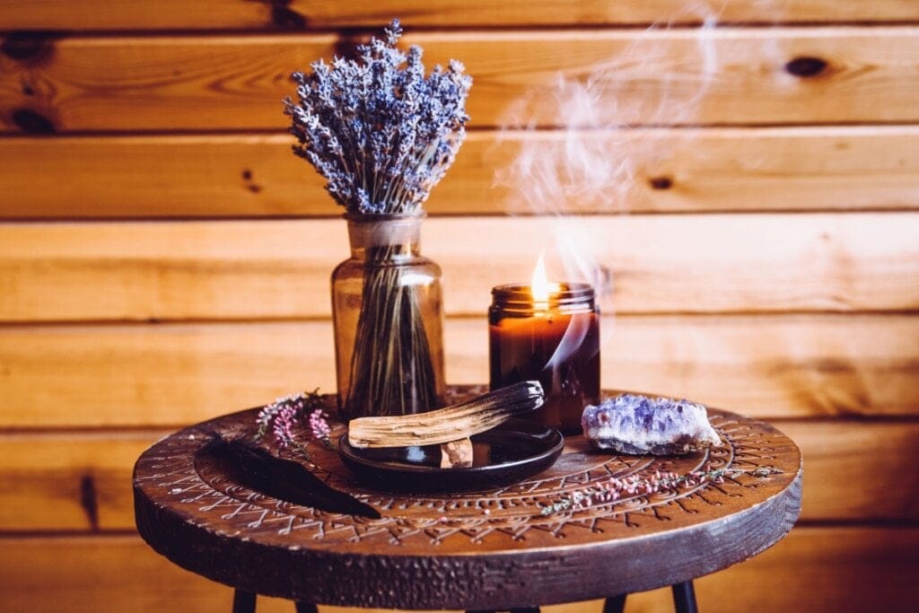 Incenso de lavanda queimando apoiado em tigela em cima de mesa de madeira, com um vaso com lavanda e uma vela acesa e um cristal