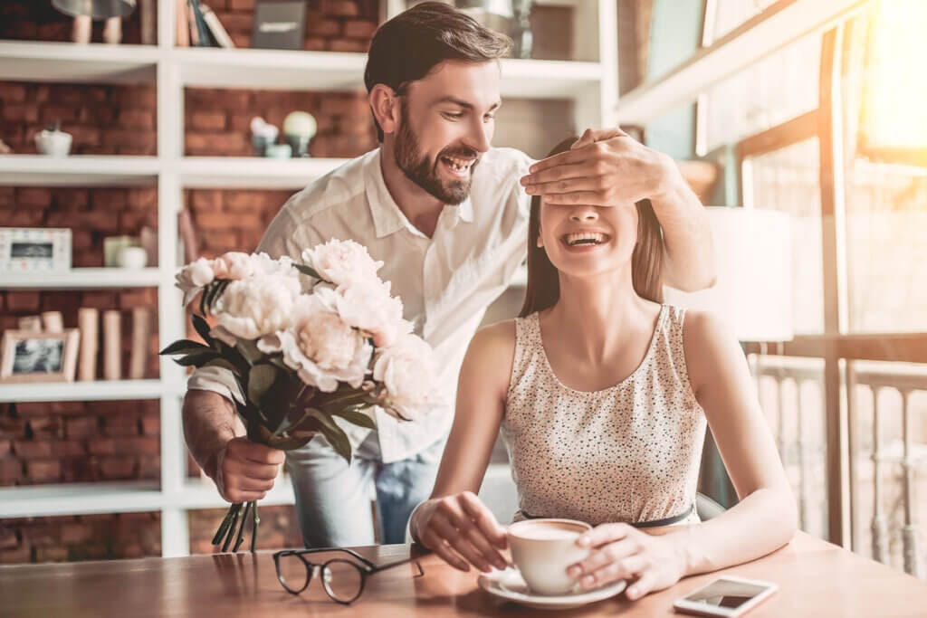 Casal romântico no café. Homem fazendo surpresa com flores à namorada.