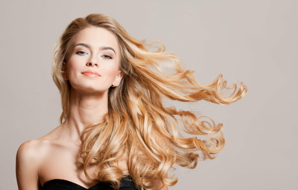 Mulher com cabelo loiro claro ondulado comprido e usando top preto em fundo bege