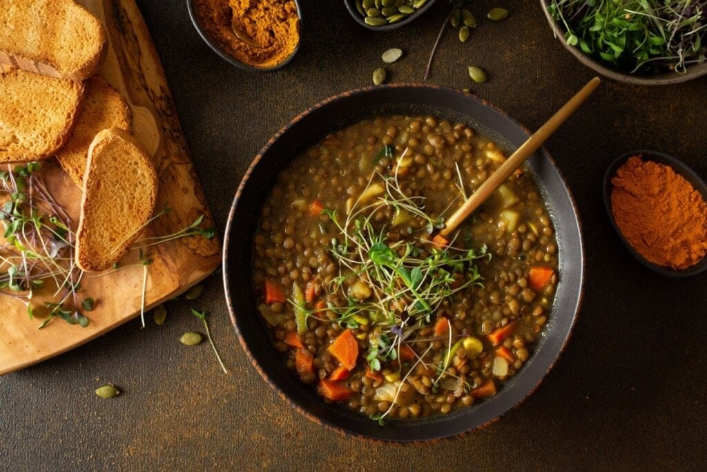 Recipiente preto com sopa de lentilha com batata, cenoura, salsinha e brotos