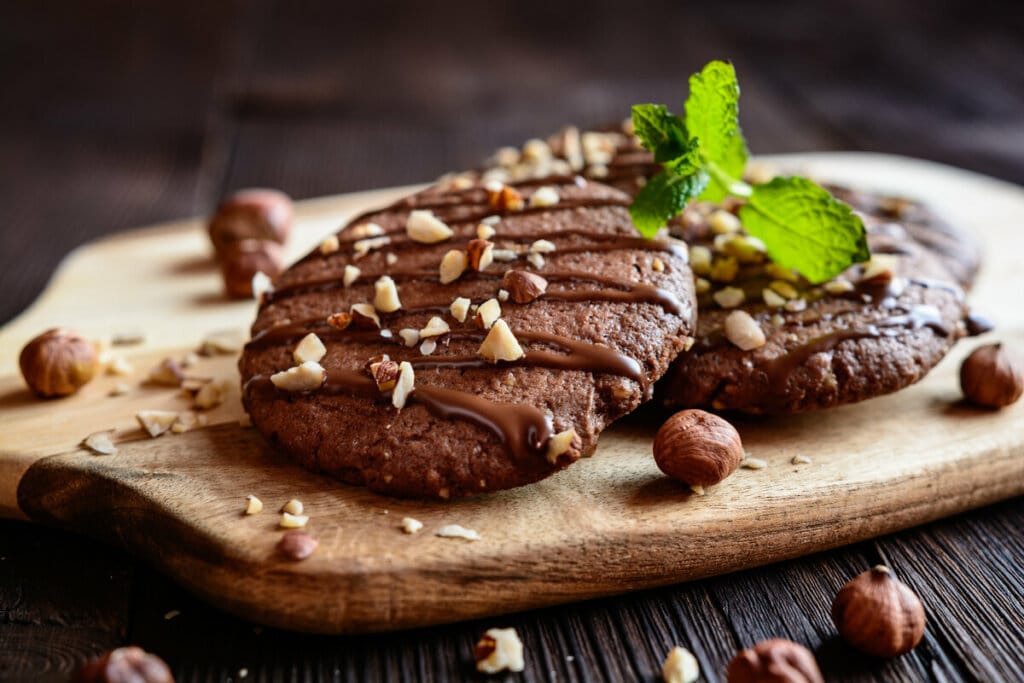 Dois biscoitos de chocolate em cima de uma tábua decorados com avelãs trituradas e folhas de hortelã