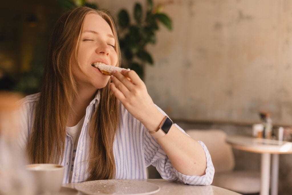 Mulher sentada, comendo pão com os olhos fechados 