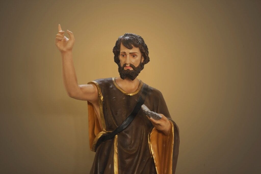 Estátua de São João com a mão levantada para cima, cabelos longos e barba 