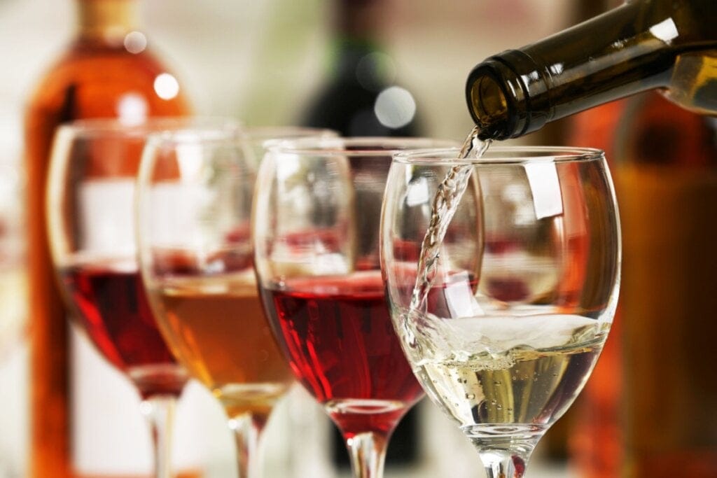Taças enfileiradas com vinhos em diferentes tons, como tinto e branco