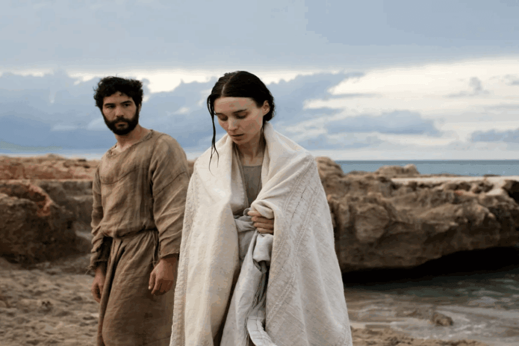 Imagem de um homem e uma mulher usando roupas de época, o homem está de marrom e tem o cabelo curto e barba e está com uma expressão apreensiva e a mulher está usando roupas bege, com o cabelo molhado e enrolada em um pano