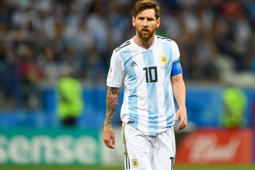 Homem com cabelo curto e barba usando uniforme de futebol branco e azul