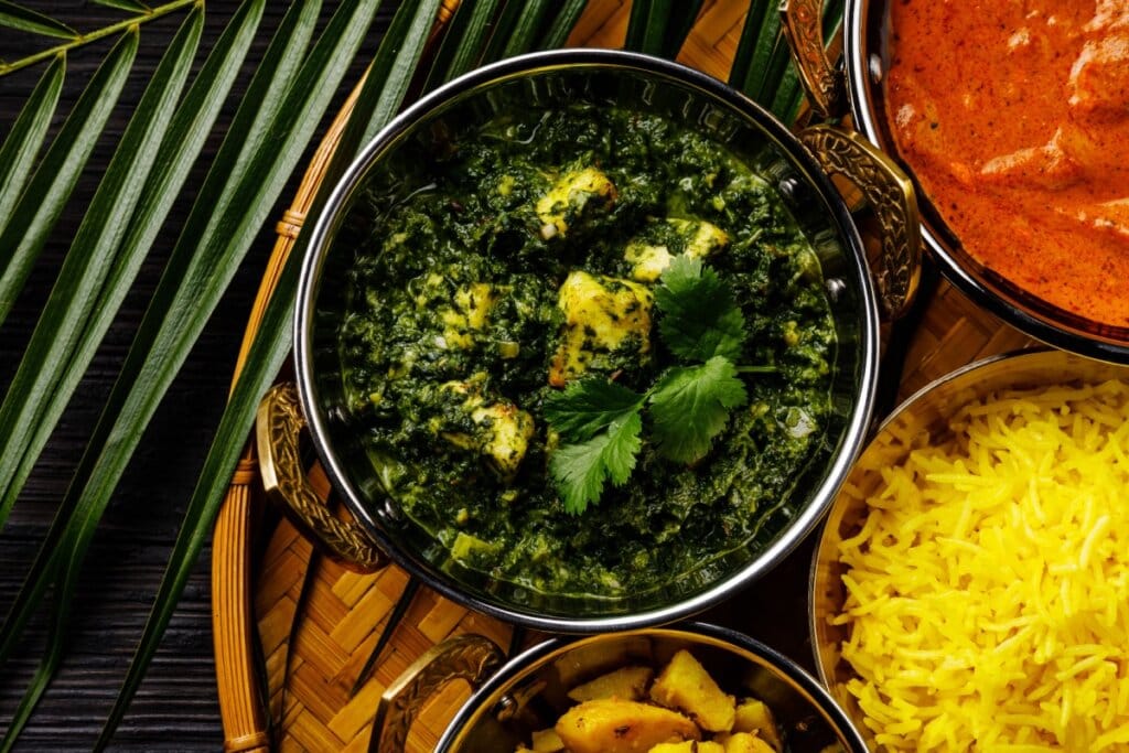 Frango ao curry com ora-pró-nóbis em recipiente em bandeja de madeira em cima de mesa de madeira