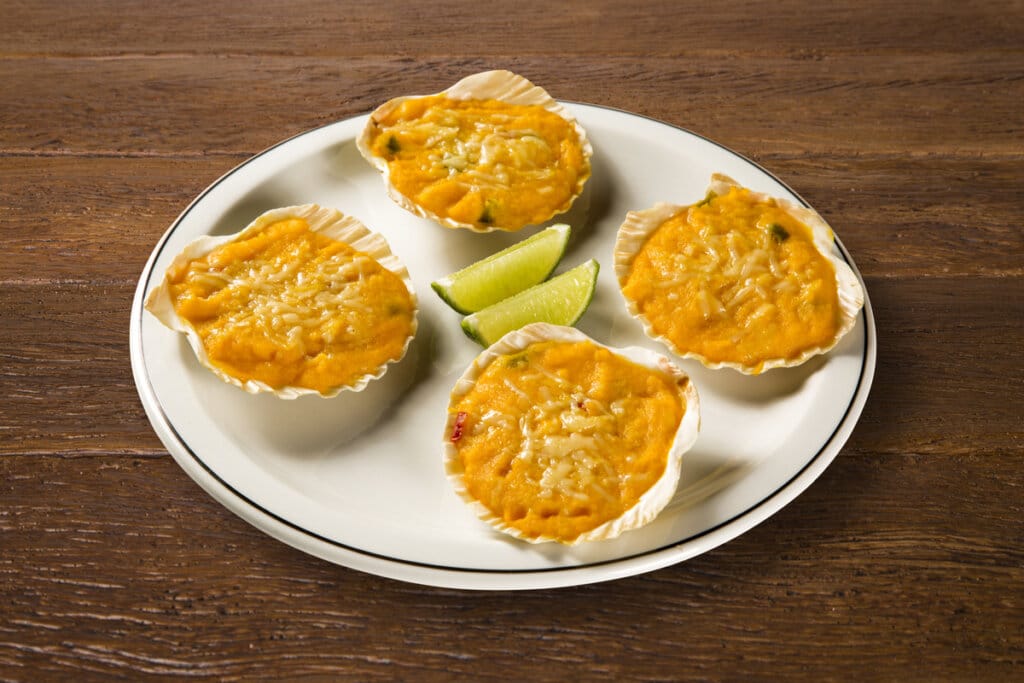 4 casquinhas de siri servidas em um prato branco com limões 