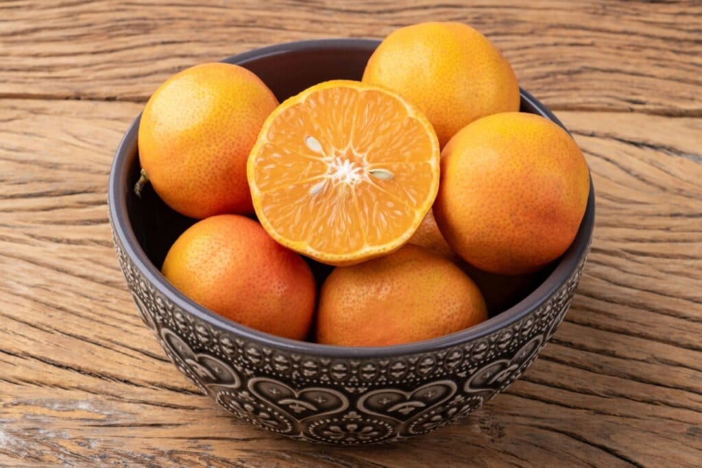 Limão-cravo dentro de tigela de cerâmica em cima de mesa de madeira um deles está cortado na metade