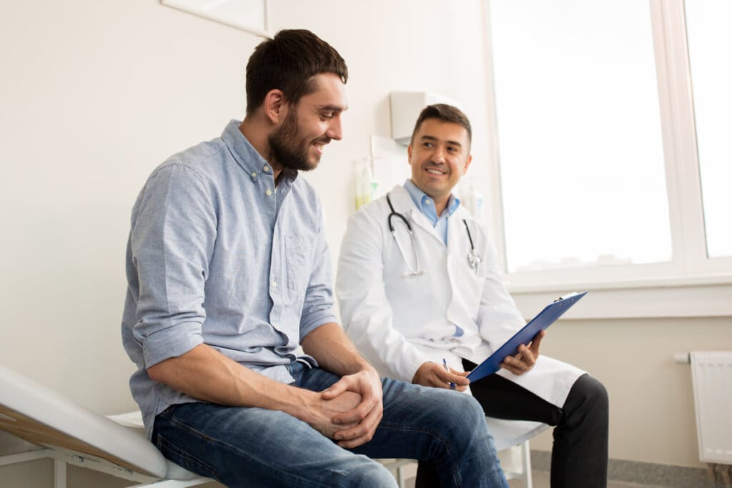 Homem em consulta médica; o paciente e o profissional estão sentados em maca