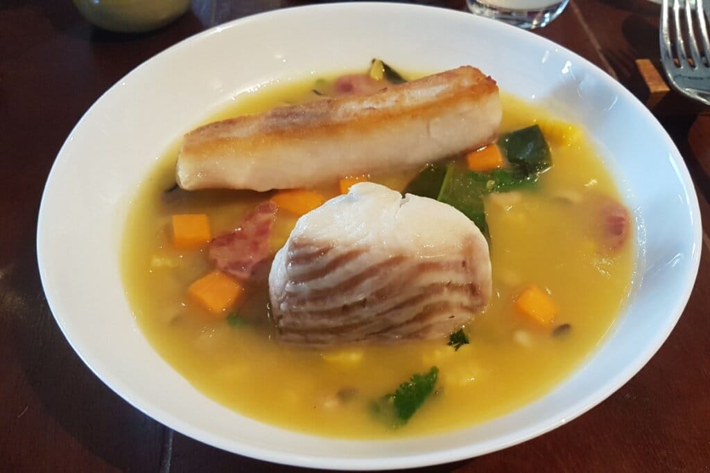 peixe ao molho de tucupi servido em prato fundo branco em cima de mesa de madeira