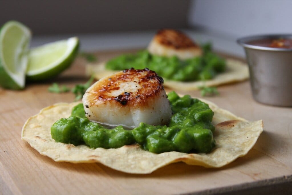 Taco de vieira com molho de ervilha em cima de uma tábua de madeira 
