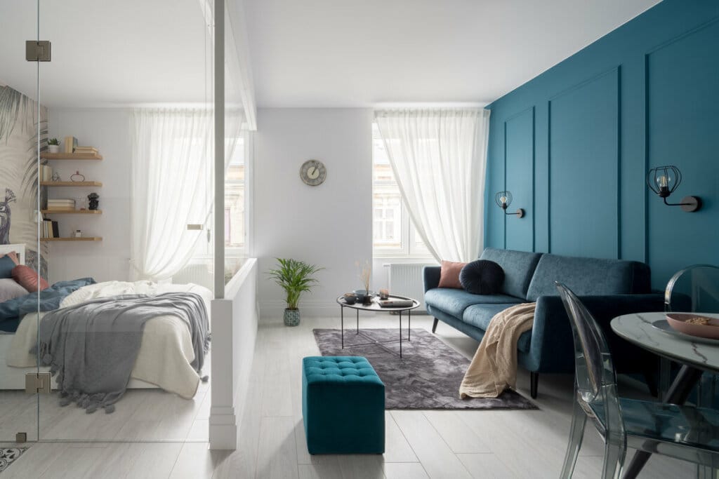 Apartamento com parede e sofá verde, cortina branca e espelhos