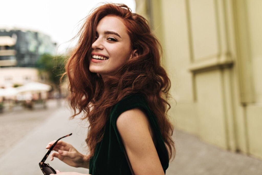Mulher com cabelo ruivo escuro profundo caindo no rosto e sorrindo