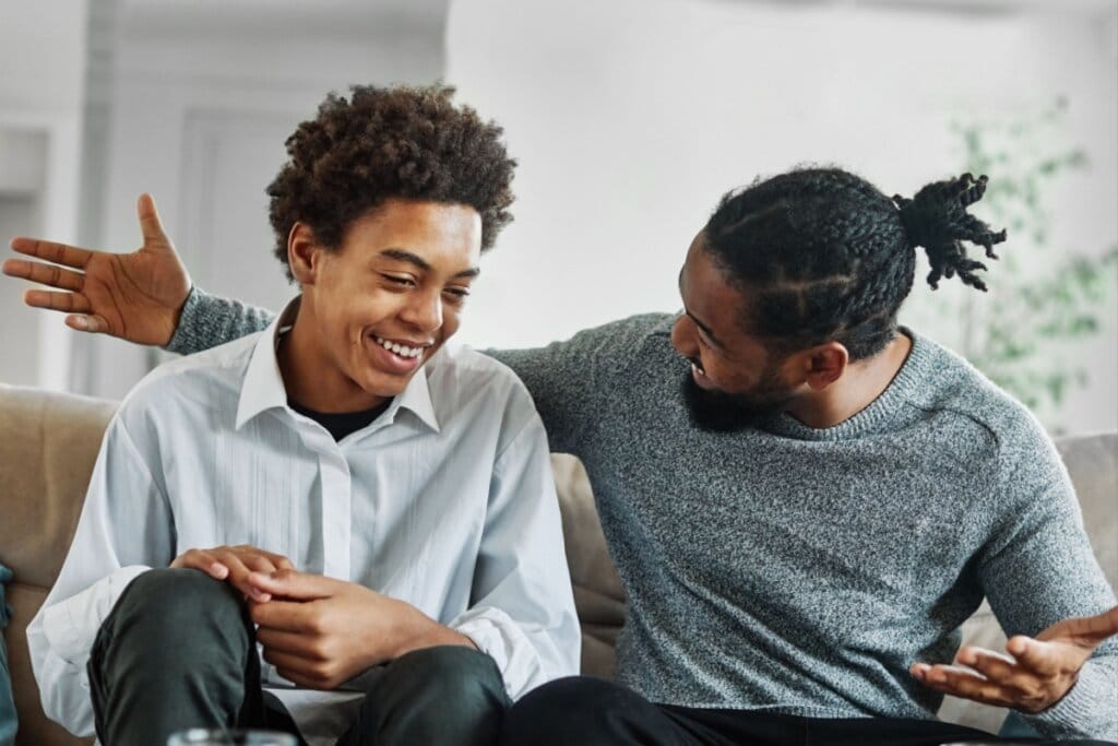 Jovem menino e um homem sentado em um sofá conversando e sorrindo