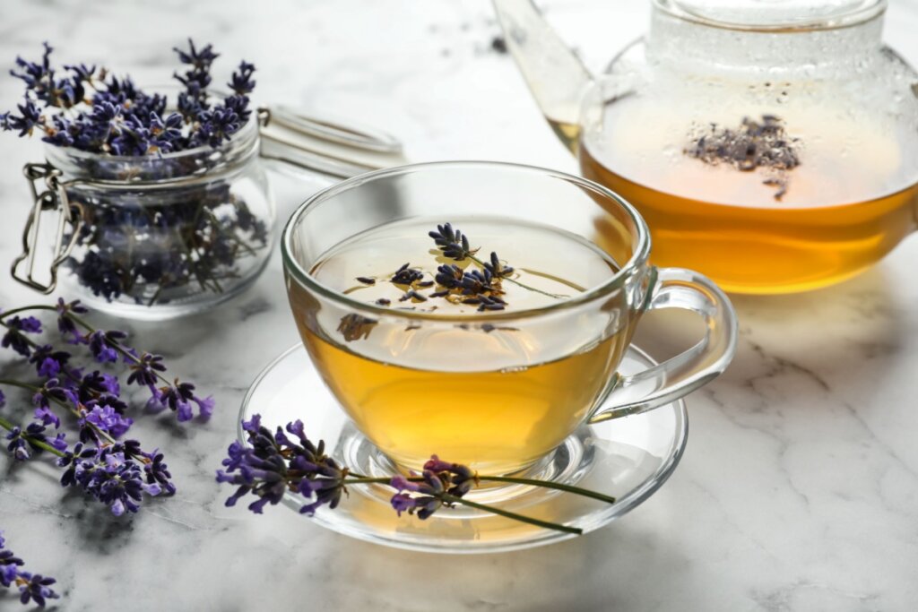 Chá de lavanda servido em copo e bule de vidro com flores de lavanda ao lado