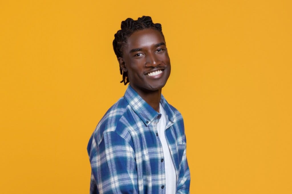 homem negro de camisa xadrez azul com cabelo trançado em fundo amarelo