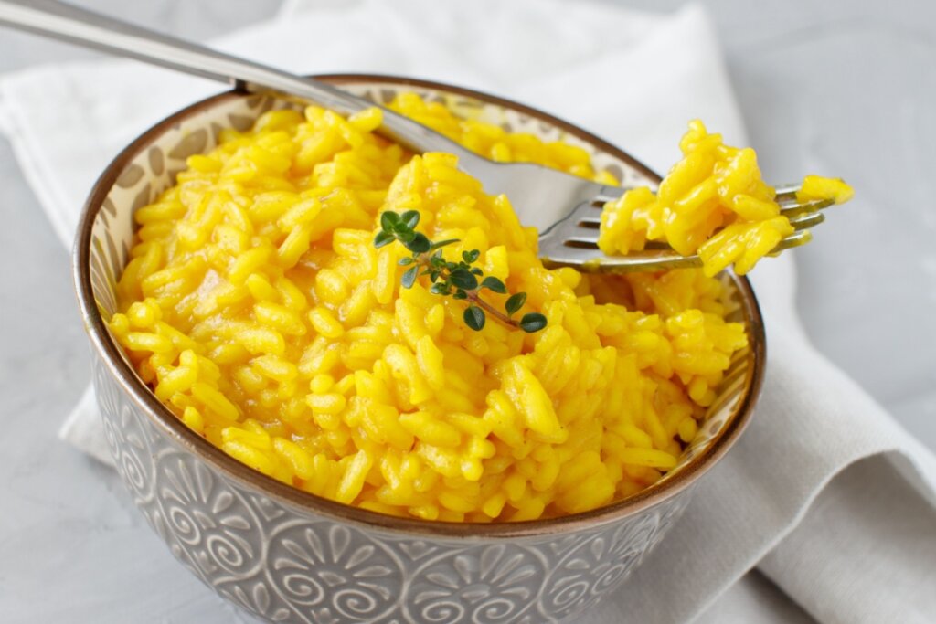 Risoto de cúrcuma cremoso servido em tigela de cerâmica estampada em cima de mesa de madeira com guardanapo e garfo