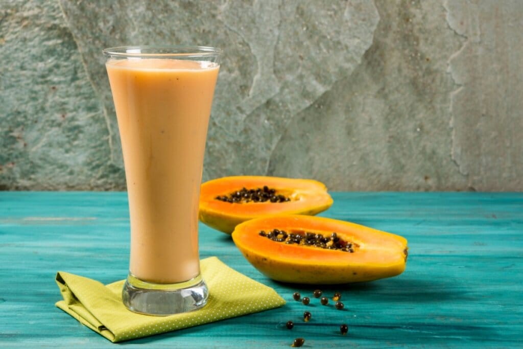 copo longo com vitamina laranja e duas fatias de mamão ao fundo