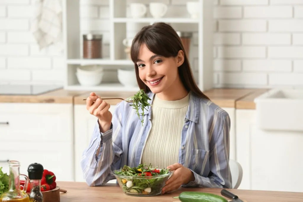 Mulher sentada em uma cozinha, comendo salada em um recipiente de vidro