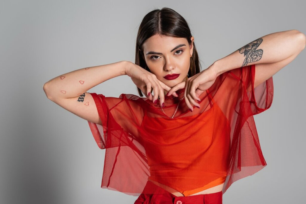 Mulher com as duas mãos no queixo vestindo blusa vermelha transparente