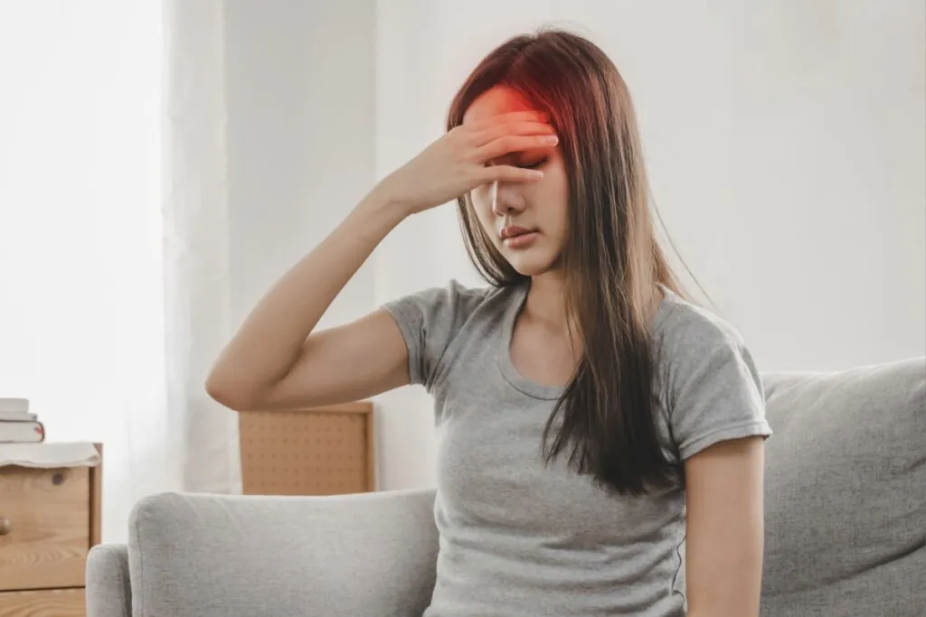 Mulher sentada, com a mão apoiada na testa e os olhos fechados, com a ilustração de uma mancha vermelha na cabeça