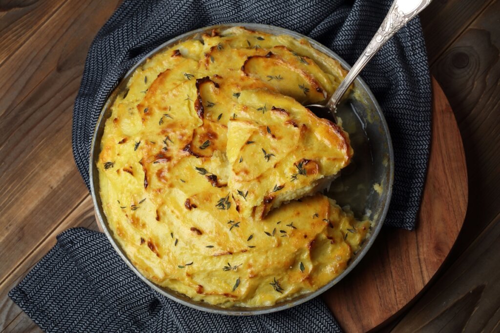 Gratinado de peixe com batatas  em forma e colher com um pedaço do prato