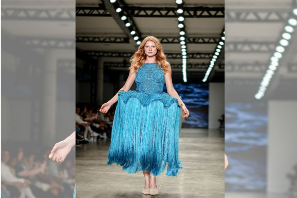 modelo de cabelo ruivo ondulado e vestido azul com saia rodada de linha andando em passarela