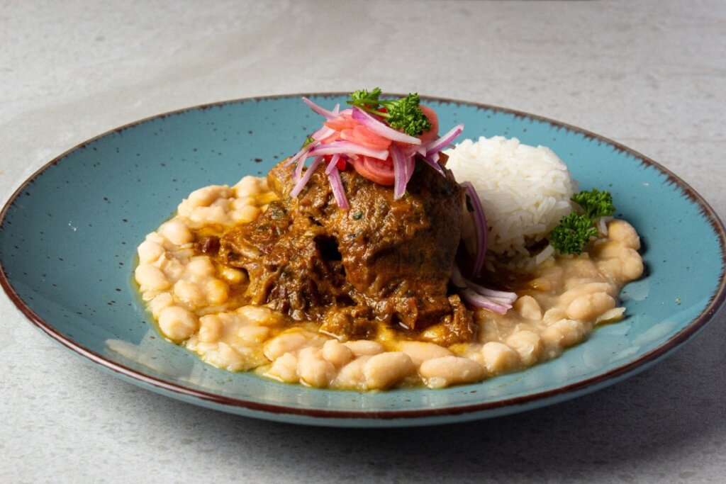Prato com carne ao molho servida sobre creme de grão-de-bico, acompanhada de arroz branco e cebola-roxa marinada