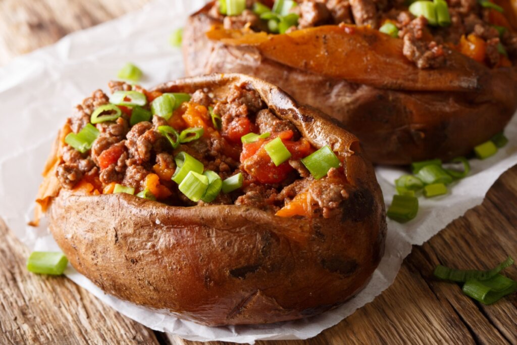 Batata-doce recheada com carne moída e tomate em cima de guardanapo, em cima de mesa de madeira
