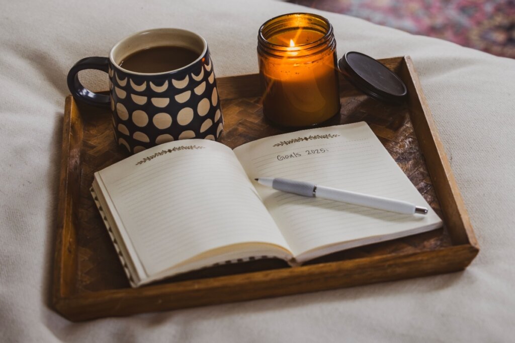 Caderno aberto com caneta, uma xícara de café e uma vela acesa sobre uma bandeja de madeira