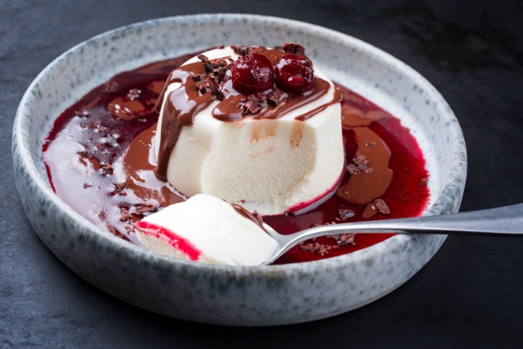 Panna cotta de amêndoas com creme de chocolate e calda de cereja em um prato cinza fundo