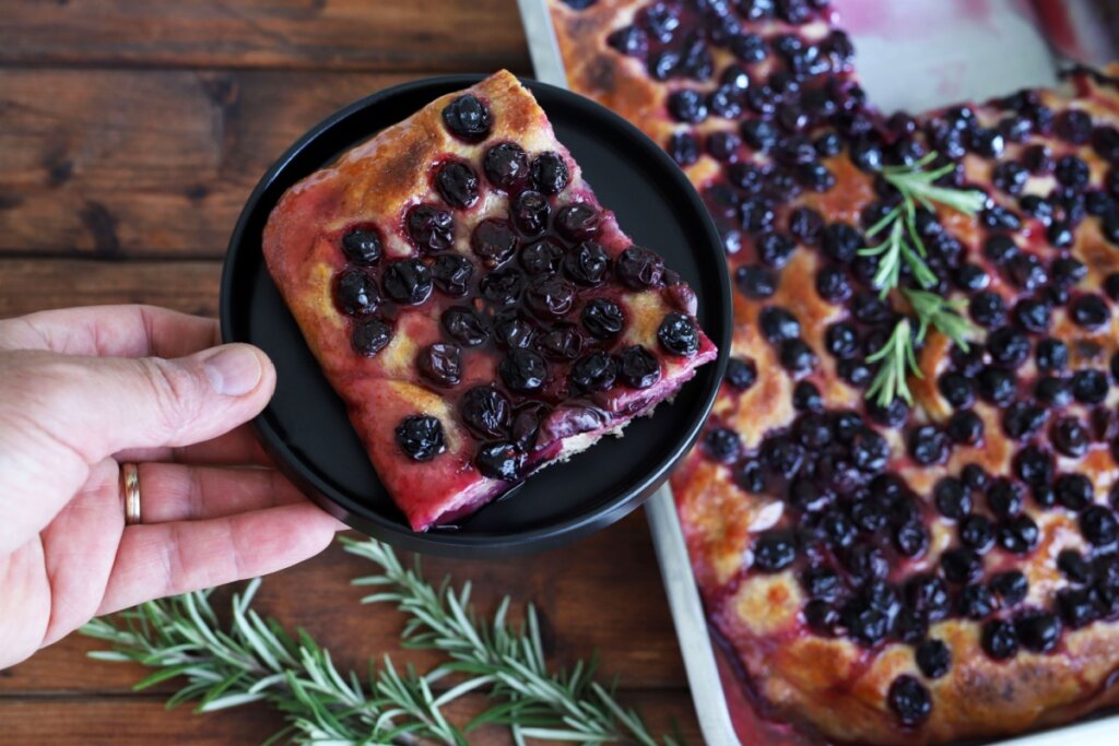 Mãos de uma pessoa segando um prato com um pedaço de focaccia rústica de uva (Schiacciata all'Uva) 