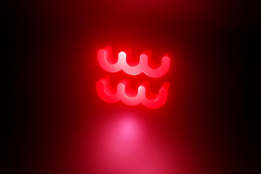 Ilustração em vermelho do símbolo do signo de Aquário em fundo vermelho escuro