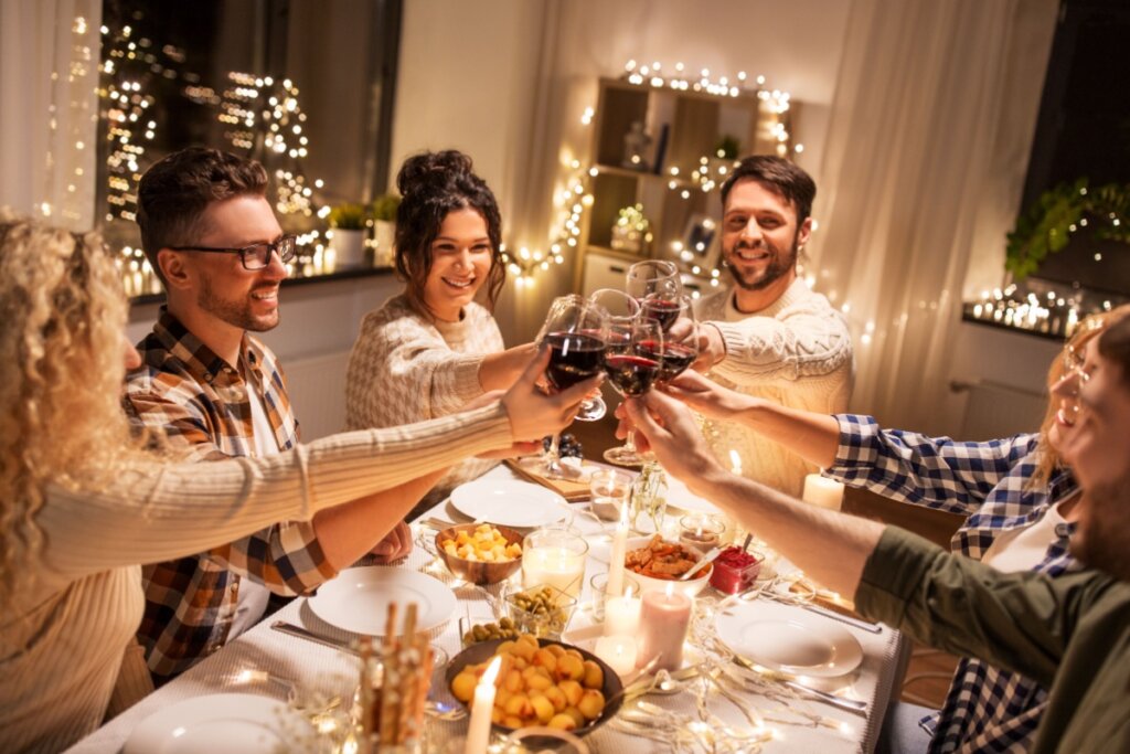 seis pessoas, homens e mulheres, sentados à mesa e brindando com taça de vinho